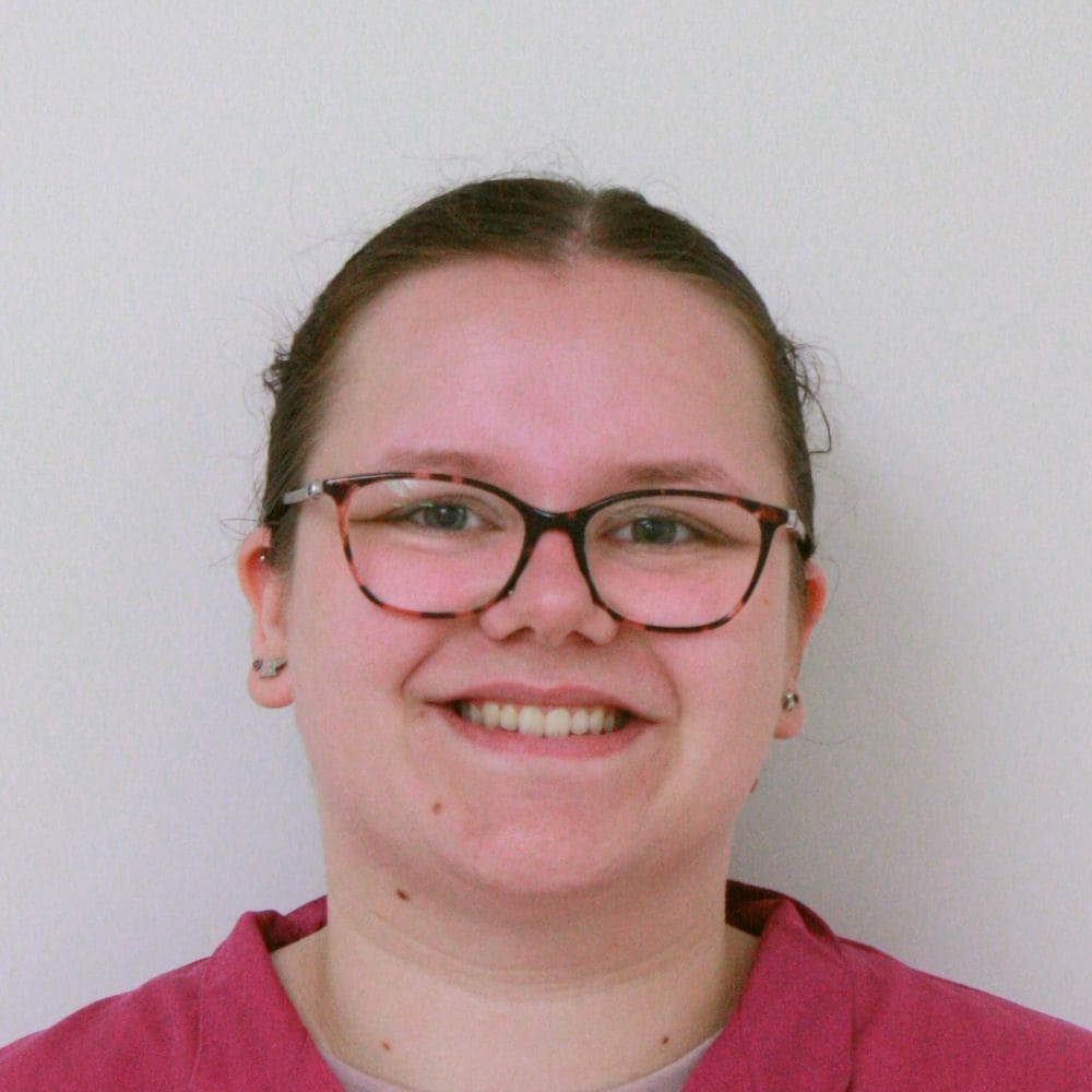 Portret van een medewerker van de kliniek met bril en roze werkkleding